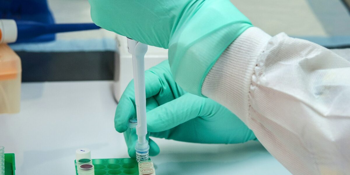 Pesquisador com luvas manipula pipeta e frasco em bancada de laboratório