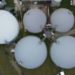 Grandes tanques brancos de biodigestão em meio a um campo verde