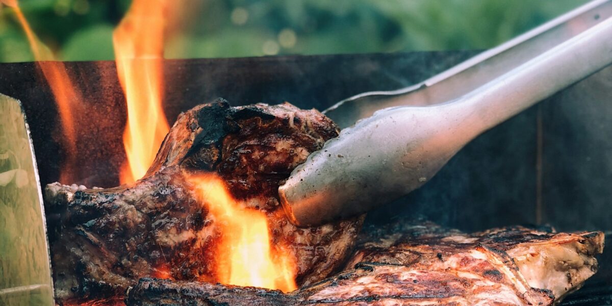 Pinça de metal virando carne grelhada sobre o fogo