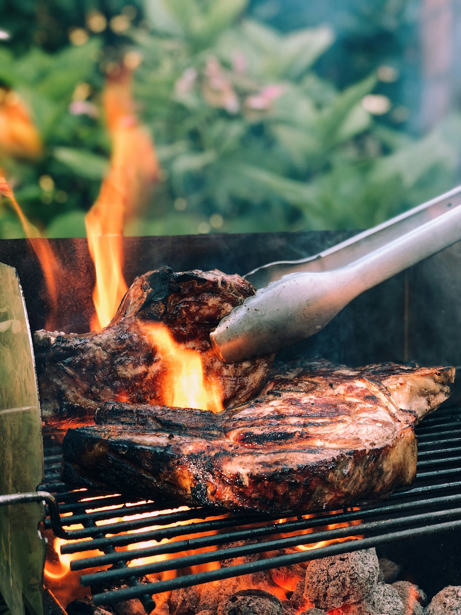 Pinça de metal virando carne grelhada sobre o fogo
