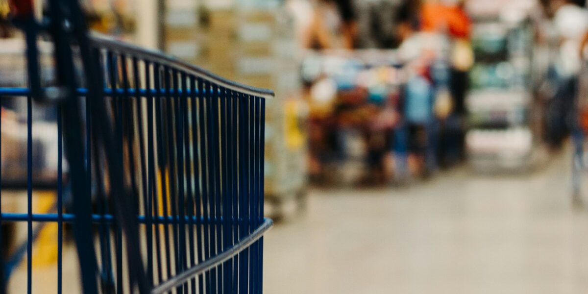 Grupo Pereira, com matriz em Campo Grande, compra 21 lojas do Carrefour e leva o Comper a São Paulo 1 Carrinho de compras azul em corredor de supermercado desfocado
