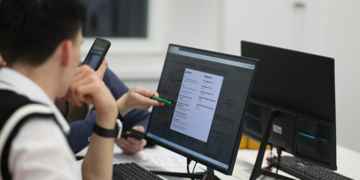 Grupo de pessoas sentadas a uma mesa utilizando computadores em ambiente de curso