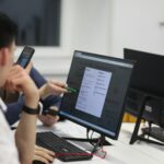 Grupo de pessoas sentadas a uma mesa utilizando computadores em ambiente de curso