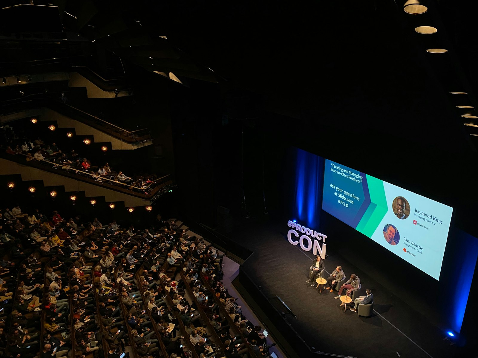 Painel de discussão em palco de auditório diante de plateia