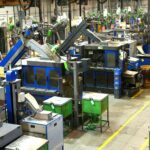Vista do chão de uma fábrica com máquinas industriais e faixas amarelas de sinalização