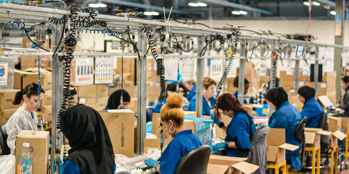 Indústria de MS opera com quase 30% de capacidade ociosa e adia contratações 1 Trabalhadores de uniforme azul operando uma linha de montagem em uma fábrica