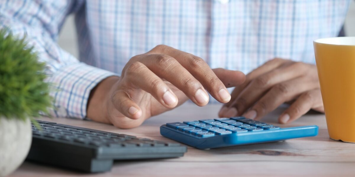Pessoa usando calculadora sobre uma mesa de trabalho ao lado de uma caneca de café