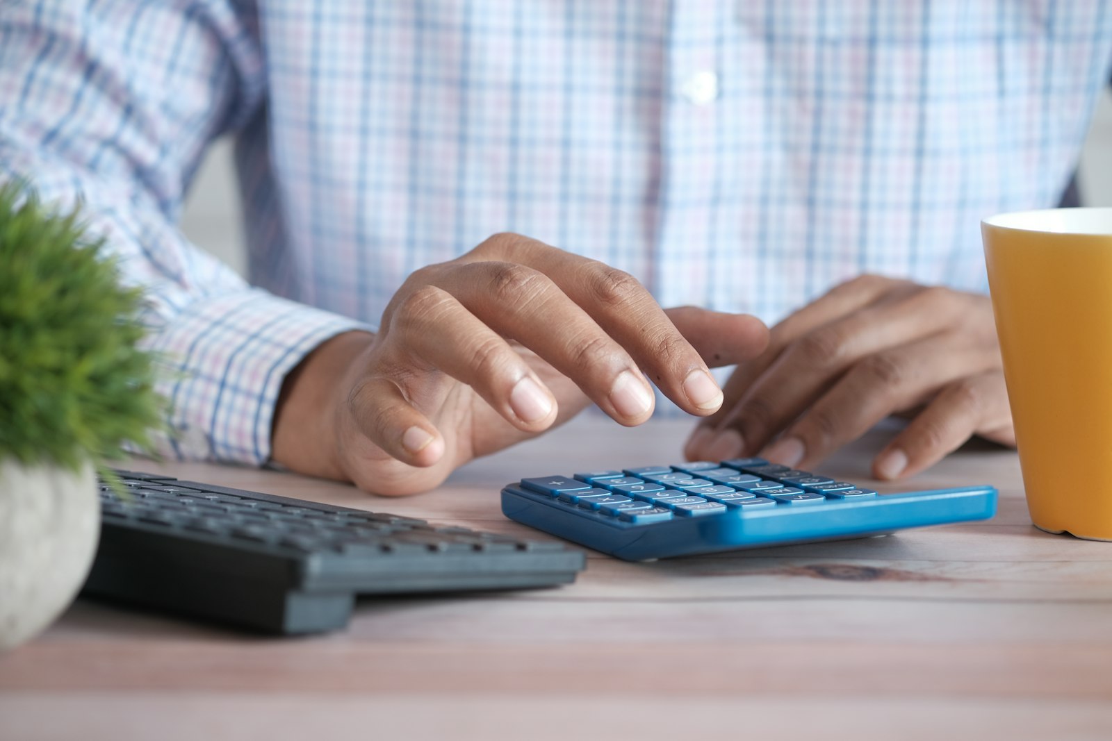 Pessoa usando calculadora sobre uma mesa de trabalho ao lado de uma caneca de café
