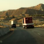 Caminhões de carga circulando por uma rodovia em paisagem montanhosa e árida