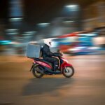Entregador em scooter vermelha circulando por rua de cidade à noite