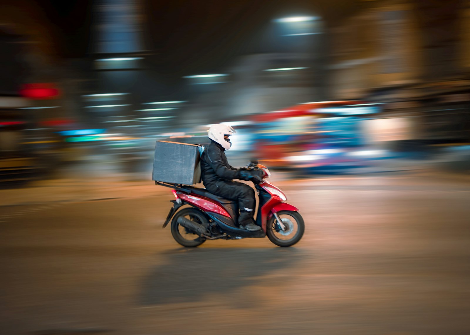 Entregador em scooter vermelha circulando por rua de cidade à noite