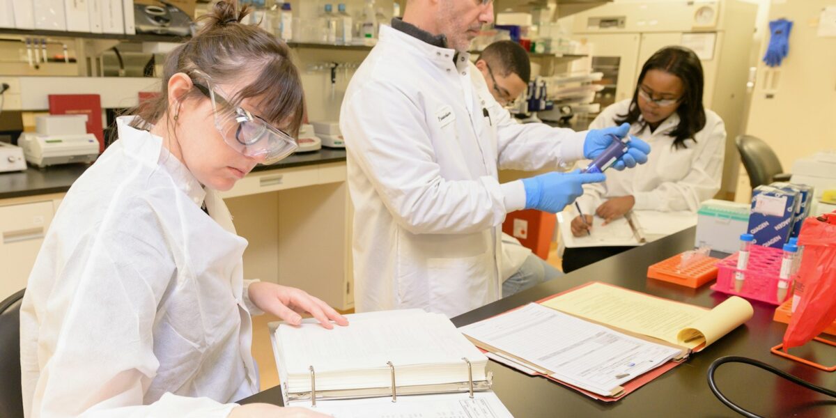 Grupo de pessoas de jaleco trabalhando em bancada de laboratório