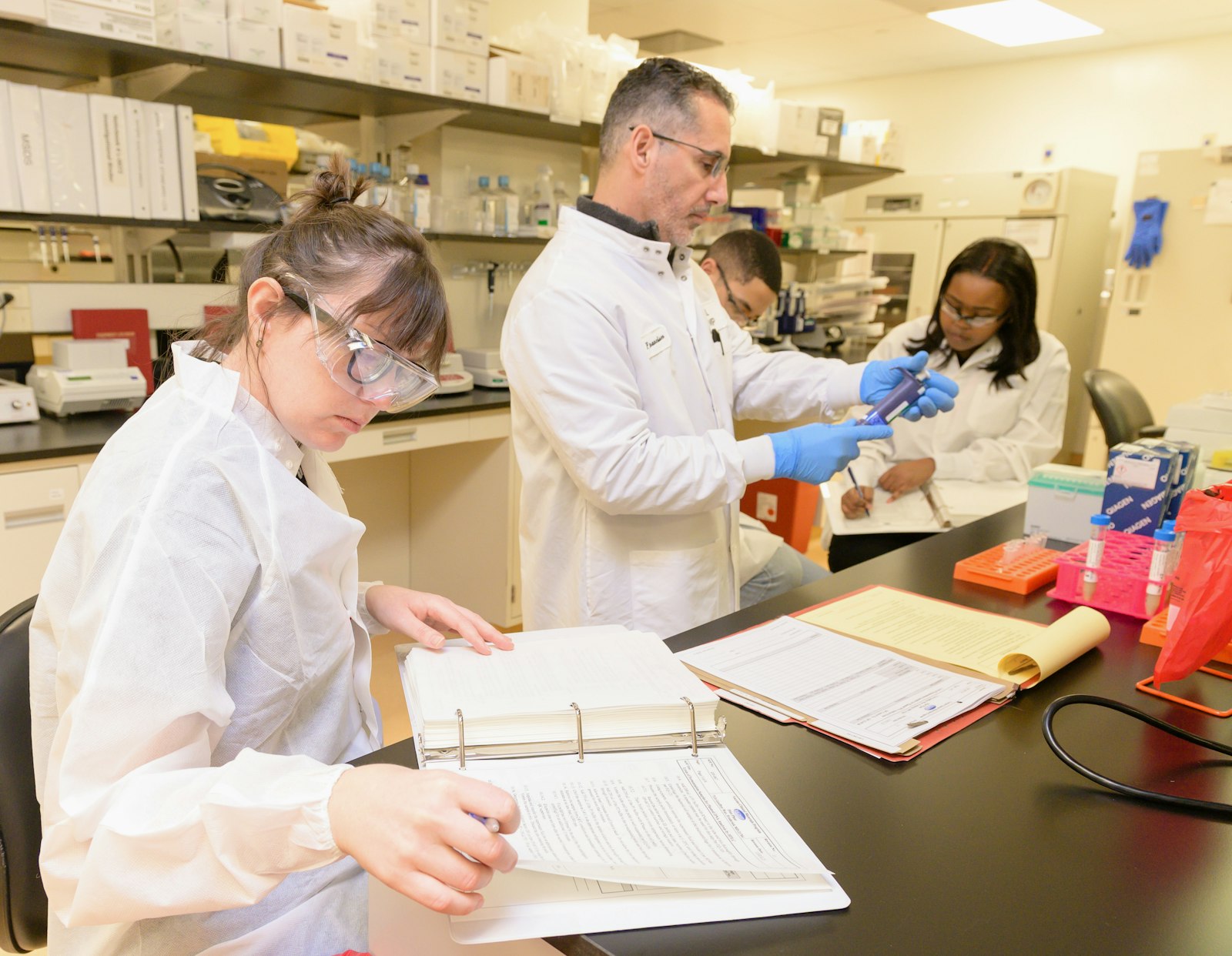 Grupo de pessoas de jaleco trabalhando em bancada de laboratório