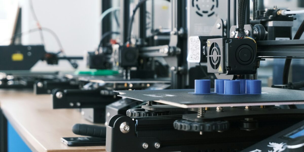 Fileira de impressoras 3D criando peças plásticas azuis sobre uma bancada de madeira