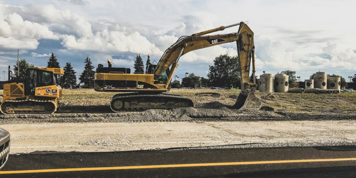Escavadeira amarela movimentando terra em obra de terraplenagem