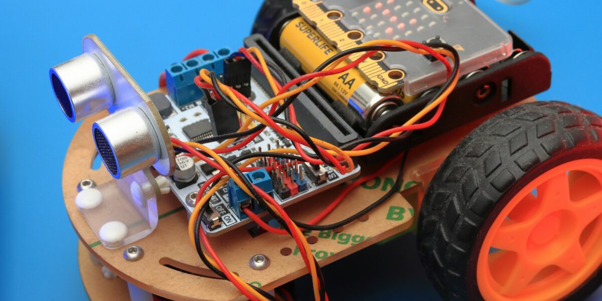 Pequeno carro robô com rodas, placa eletrônica e fios sobre uma mesa