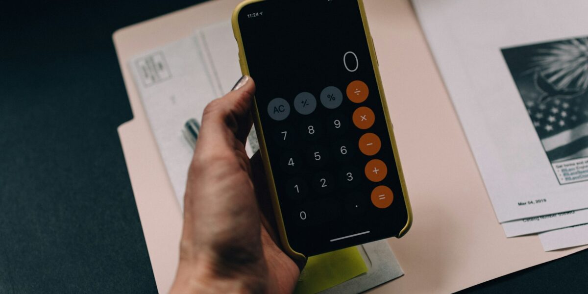 Mão segurando smartphone com aplicativo de calculadora sobre pasta de documentos