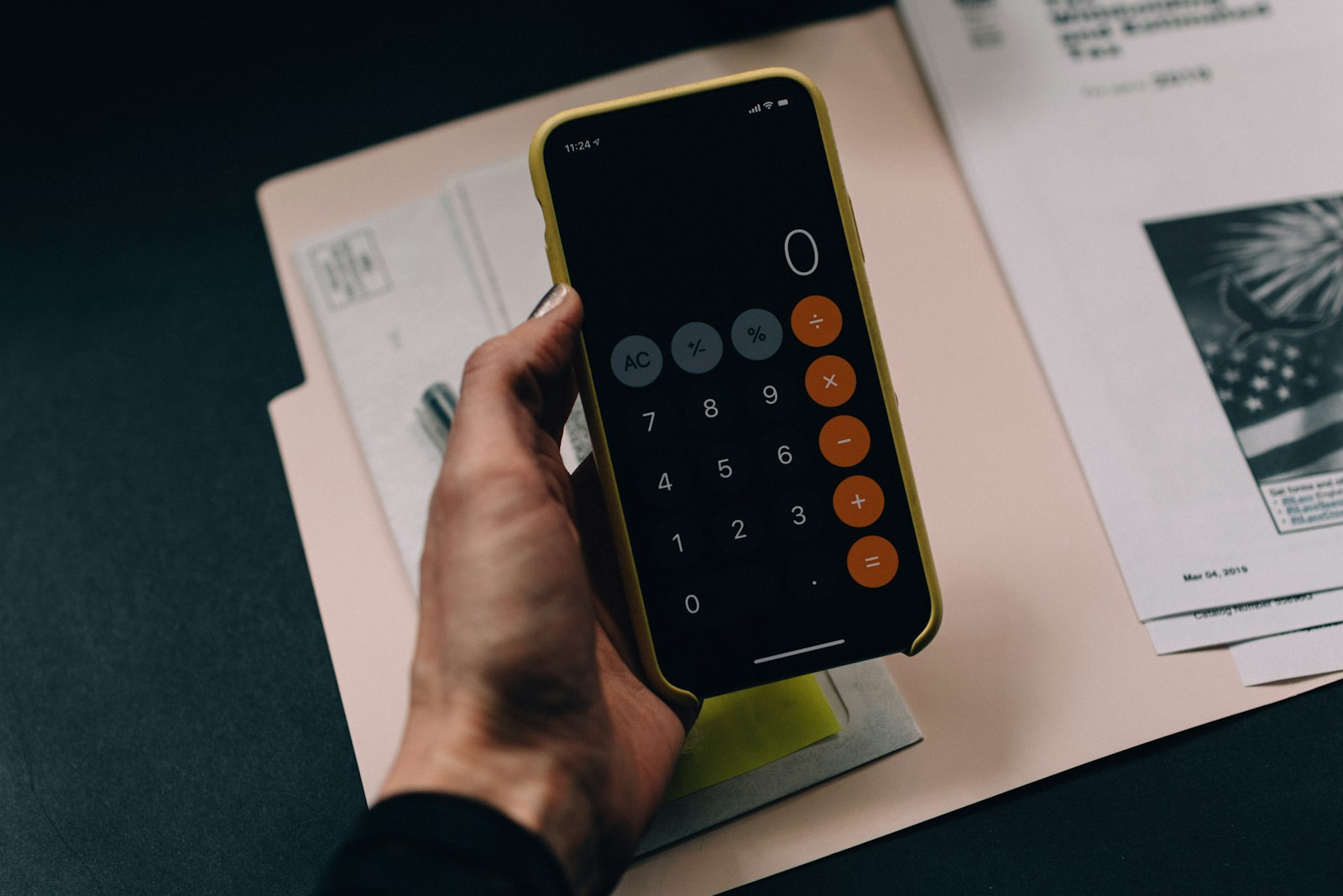 Mão segurando smartphone com aplicativo de calculadora sobre pasta de documentos