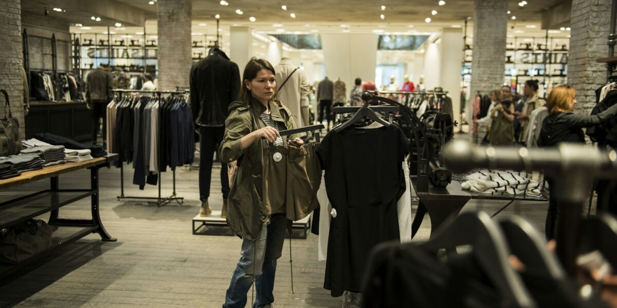 Campo Grande terá mil vagas temporárias no fim do ano; veja como disputar e seus direitos 1 Mulher segura peças de roupa dentro de uma loja de vestuário